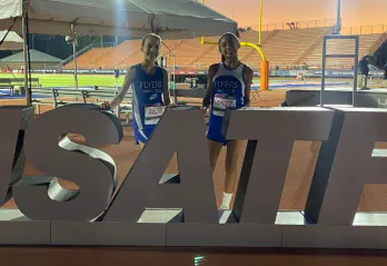 Flyers athletes pose at track in front of USATF sign.