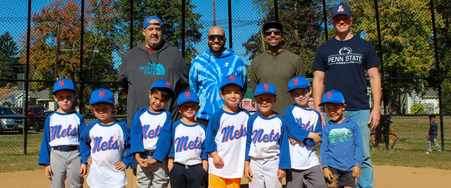 Mets T-Ball team smiling for a picture with their four coaches.