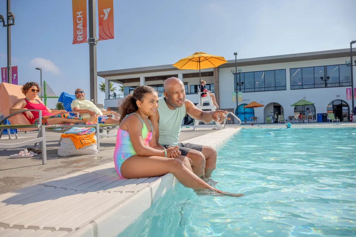 Father and Daughter Sit on the ledge of an outdoor pool
