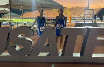 Flyers athletes pose at track in front of USATF sign.